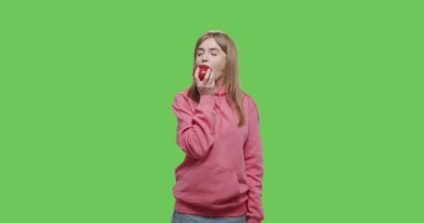 Młoda kobieta je duże czerwone jabłko na tle klucza chroma — Wideo stockowe