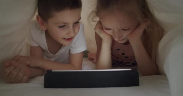 Garçon et fille couché sous la couverture avec tablette — Video