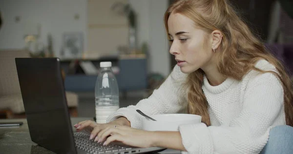 Ung kvinna som använder telefon och dator i hemmet — Stockfoto