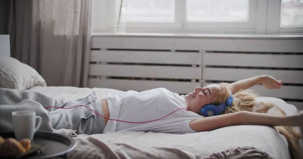 Νεαρή γυναίκα που χρησιμοποιεί έξυπνο τηλέφωνο ξαπλωμένη στο κρεβάτι — Φωτογραφία Αρχείου