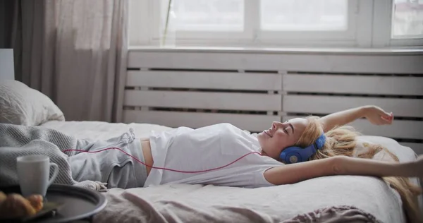 Jovem mulher usando telefone inteligente deitado na cama — Fotografia de Stock