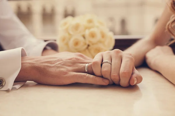 Ένα παντρεμένο ζευγάρι εκμετάλλευση εκμετάλλευση κάθε άλλο χέρι ενώ κάθεται από το τραπέζι στο καφενείο, στο φόντο της ένα μπουκέτο από λουλούδια. Κινηματογράφηση σε πρώτο πλάνο — Φωτογραφία Αρχείου
