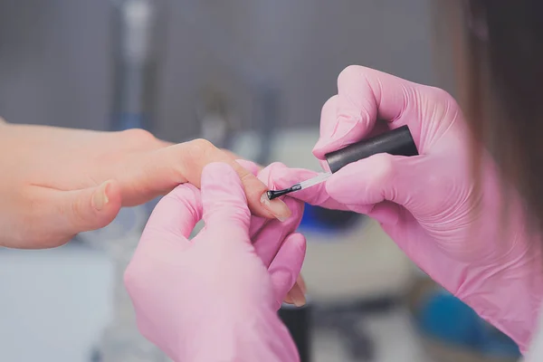 Close-up van manicure in roze rubberen handschoenen toepassen doorzichtige nagellak op vrouwelijke nagels. Professionele manicure en nagel verzorging procedure in schoonheidssalon — Stockfoto