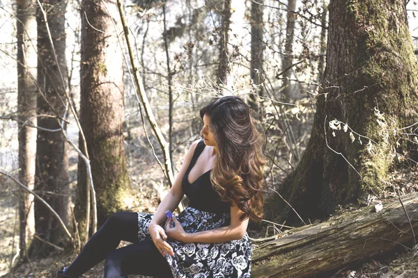 Portrait of beautiful woman with long hair in a forest sitting on a tree — Stock Photo, Image