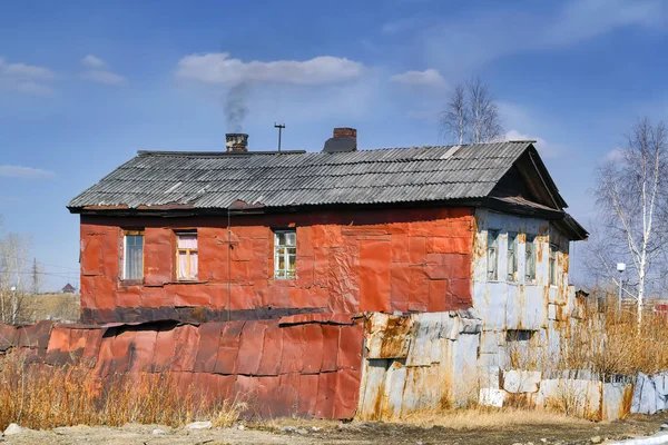 Old dilapidated colorful house studded with metal sheets with a rickety fence. — Stock Photo, Image