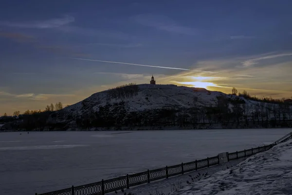 Winterlandschap eerste sneeuw op de dijk van de stadsvijver bij zonsondergang. — Stockfoto