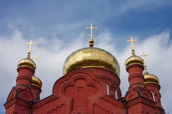 Golden domes of a red brick Christian Orthodox church against the sky.