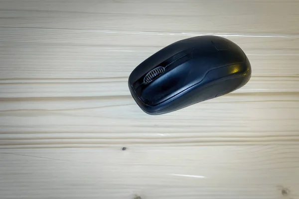 Wireless computer mouse of black color on a light wooden table.