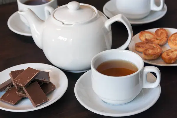 Tetera de porcelana blanca, tazas de té con té y dulces en una mesa de madera oscura . — Foto de Stock