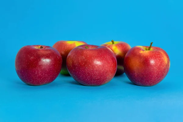 Four fresh wet red apples isolated on blue background.
