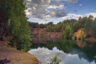 Akşamları, berrak şeffaf mavi suyla bir orman gölünün kıyısındaki manzara..