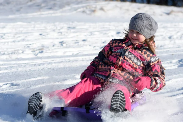 快乐的小女孩在雪地的公园里滑下山去 — 图库照片