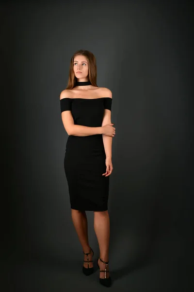 Young brunette lady in black dress posing on grey background