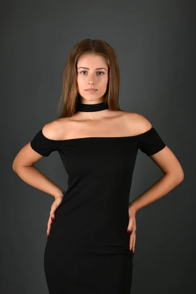 Junge brünette Dame im schwarzen Kleid posiert auf grauem Hintergrund — Stockfoto
