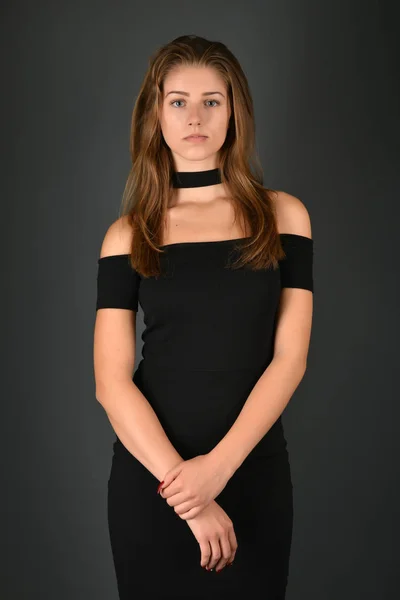 Νεαρή μελαχρινή κοπέλα σε μαύρο φόρεμα που θέτουν σε γκρι φόντο — Φωτογραφία Αρχείου