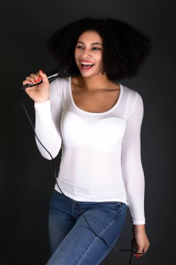 Afrikalı Amerikalı genç bir kadın mikrofonla şarkı söylüyor.