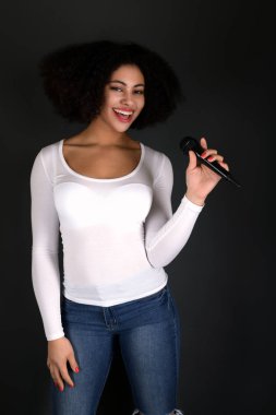 Afrikalı Amerikalı genç bir kadın mikrofonla şarkı söylüyor.