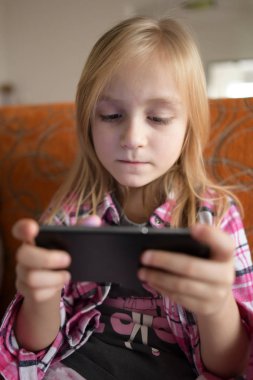 Küçük kız evde akıllı telefondan oynuyor. Cep telefonu bağımlılığı.