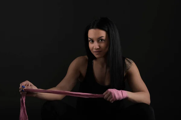 Boxing. Woman boxer sitting on bench wrapping bandage around hand close-up