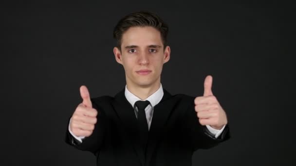 若い男が、暗い黒背景で親指を立てる — ストック動画