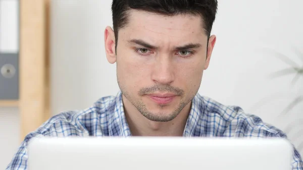 Grave giovane uomo che lavora sul computer portatile, vista frontale — Foto Stock