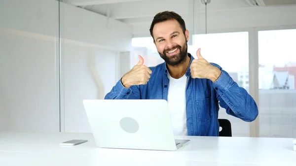 Thumbs Up by Man Sitting in Office, Looking at Camera