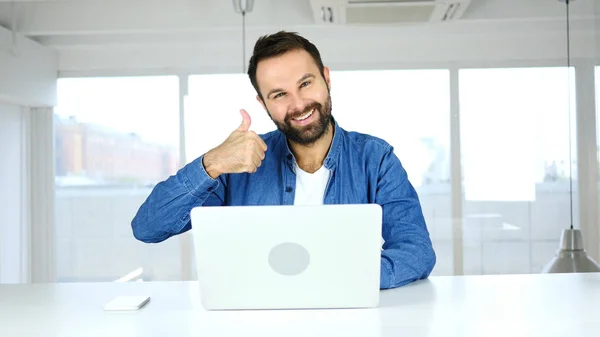 Daumen hoch von einem Mann, der im Büro sitzt und in die Kamera schaut — Stockfoto