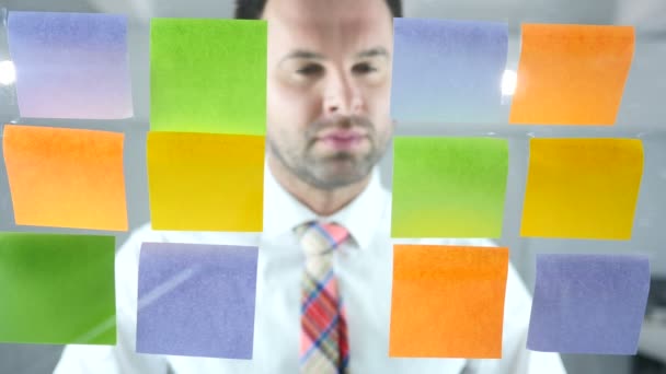 Man aan het werk op plaknotities aangesloten op glas in Office — Stockvideo