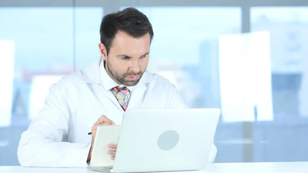 Doctor Writing Informazioni mediche del paziente, Utilizzando Laptop — Foto Stock