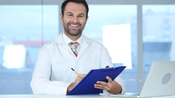 Doctor Writing Medical Reports, Sorridente verso la fotocamera — Foto Stock