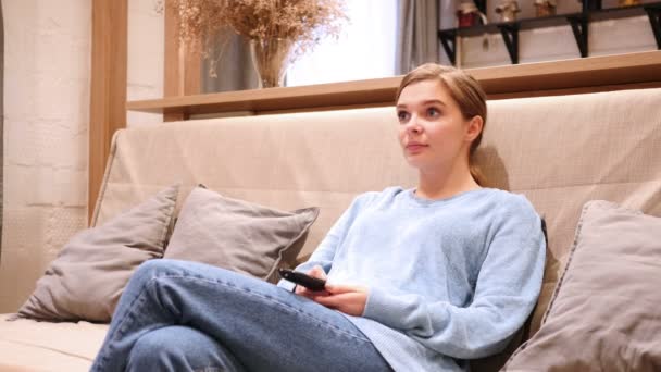 Жінка дивиться телевізор і змінює канали, сидячи на дивані — стокове відео