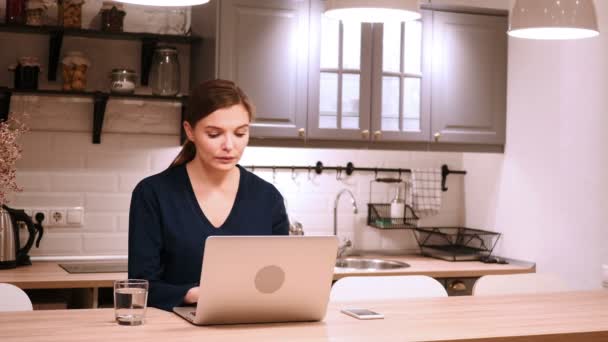 Γυναίκα γιορτάζει Online επιτυχία ενώ εργάζεστε στο φορητό υπολογιστή στην κουζίνα — Αρχείο Βίντεο