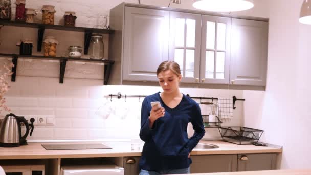 Женщина просматривает на смартфоне, набирает сообщение на кухне — стоковое видео