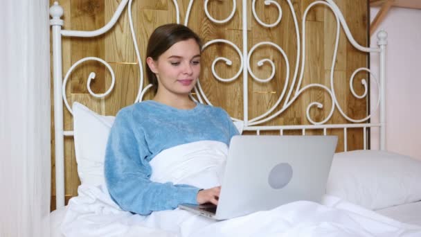 Жінка працює на ноутбуці, лежить в ліжку для відпочинку — стокове відео