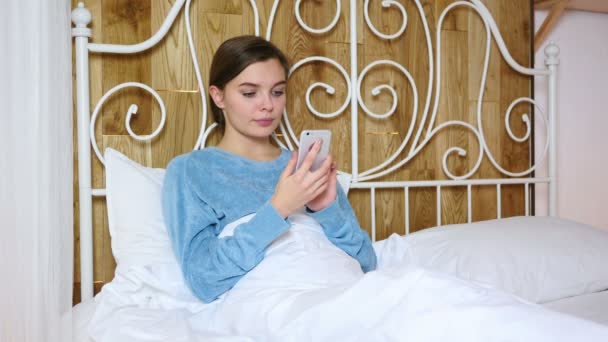 スクロールやスマート フォンで閲覧のベッドに横たわって疲れている女性 — ストック動画
