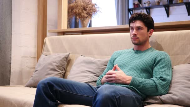 Портрет серьезного молодого человека, сидящего дома на диване — стоковое видео