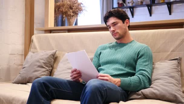 Papeleo, Hombre leyendo documentos sentado en el sofá en casa — Vídeo de stock