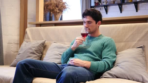 Молодой человек пьет красное вино дома, расслабляется — стоковое видео