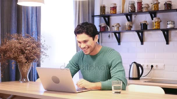 Chat vidéo en ligne par jeune homme sur ordinateur portable assis dans la cuisine — Video