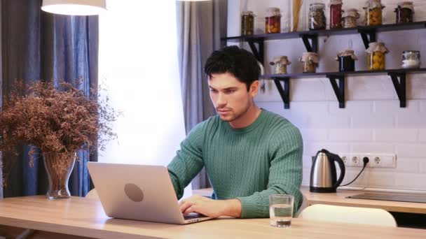 Un barbat sarbatoreste succesul in timp ce lucreaza la laptop in bucatarie — Videoclip de stoc
