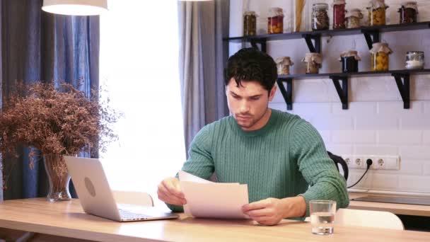 Homme travaillant sur ordinateur portable et la lecture de documents dans la cuisine, la paperasserie — Video