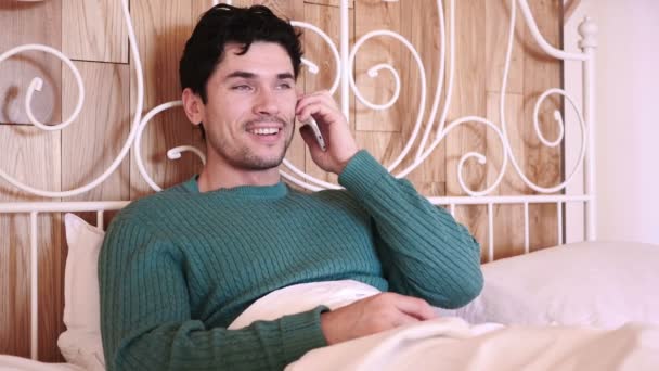 Homem sentado na cama a ligar e a falar ao telefone — Vídeo de Stock