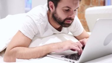 Mutlu sakal adam yatakta dizüstü bilgisayarda çalışma ve başarı için tepki,