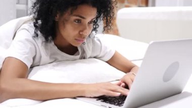 Laptop, geri kalanı için yatakta yatan çalışan Afro-Amerikan kadın