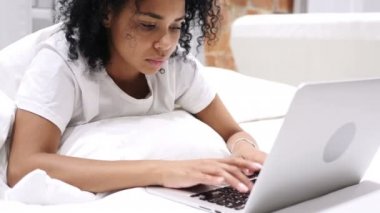 Laptop, geri kalanı için yatakta yatan çalışan Afro-Amerikan kadın