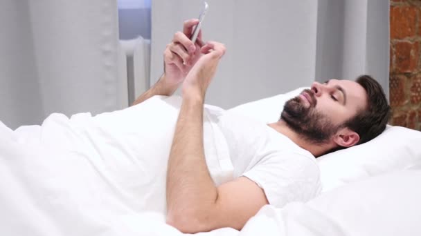 Barba Hombre en la cama Navegación en Smartphone por la noche — Vídeo de stock