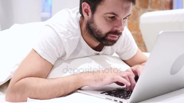 Головний біль, втомлений бородатий чоловік працює на ноутбуці в ліжку — стокове відео