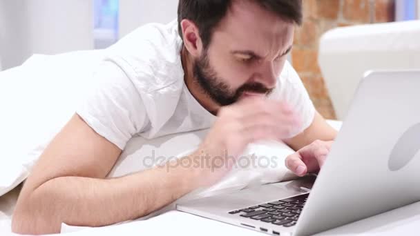 Головний біль, розроблена борода людина працює на ноутбуці в ліжку — стокове відео