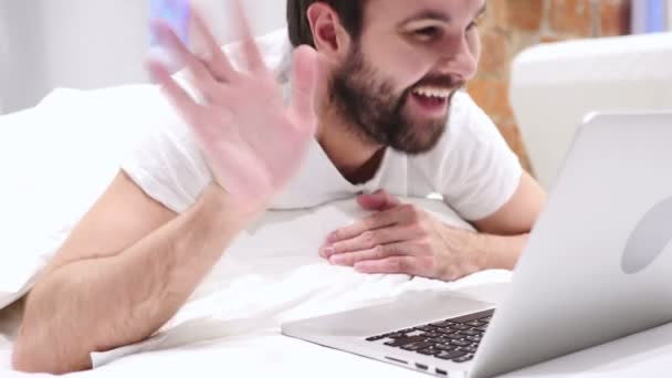 Chat de vídeo en línea por el hombre excitado acostado sobre el estómago en la cama — Vídeos de Stock