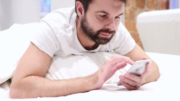 Man liggen op de maag in Bed browsen op Smartphone — Stockvideo
